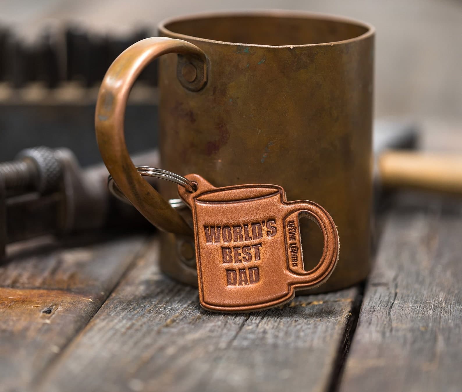 A duffle bag, dopp kit and ceramic mug sit atop a wood table in front of a wall of art prints.